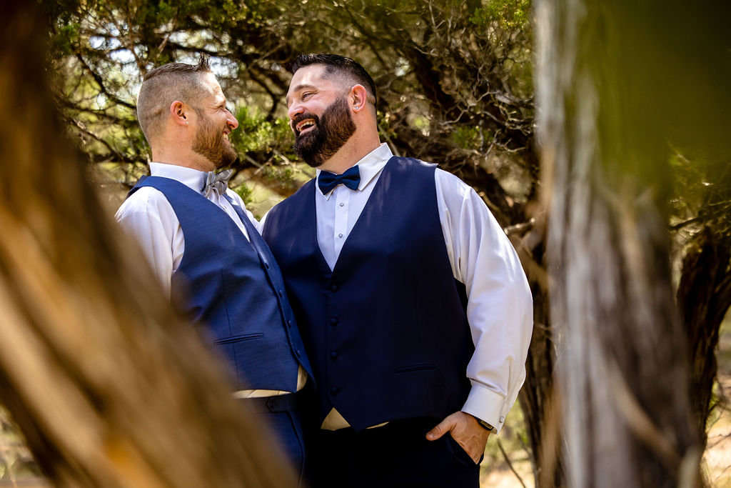 a groom laughs with his partner in some trees for their elopement photos